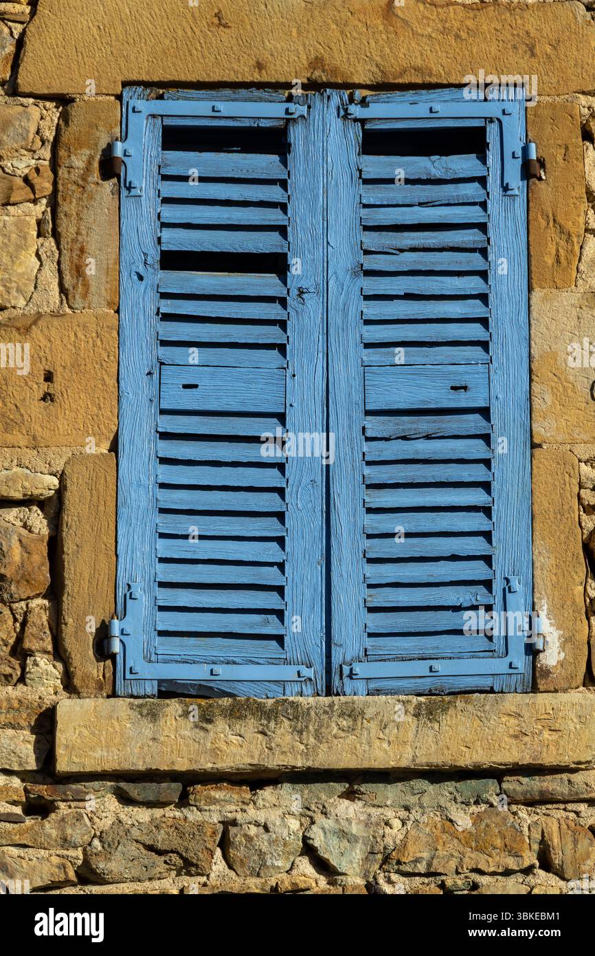 Des volets bleus vifs ornent le mur en pierre altérée d'un bâtiment traditionnel dans un village pittoresque. Auvergne, France Banque D'Images