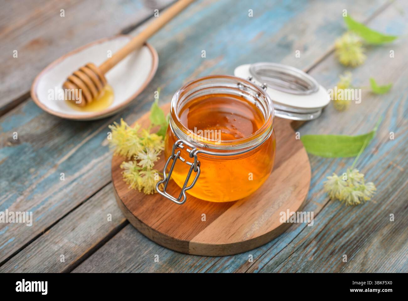 Miel de linden dans un pot en verre avec un plongeur de miel en bois et fleur de tilleul sur fond en bois Banque D'Images