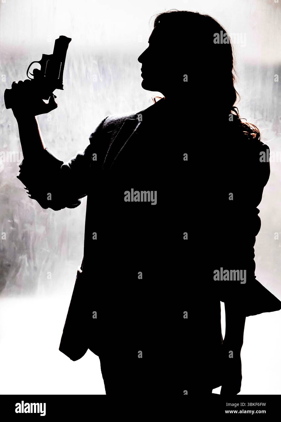 Une silhouette, probablement une femme, tient une arme de poing, suggérant une scène de danger potentiel ou d'action. L'identité de la personne et le contex spécifique Banque D'Images