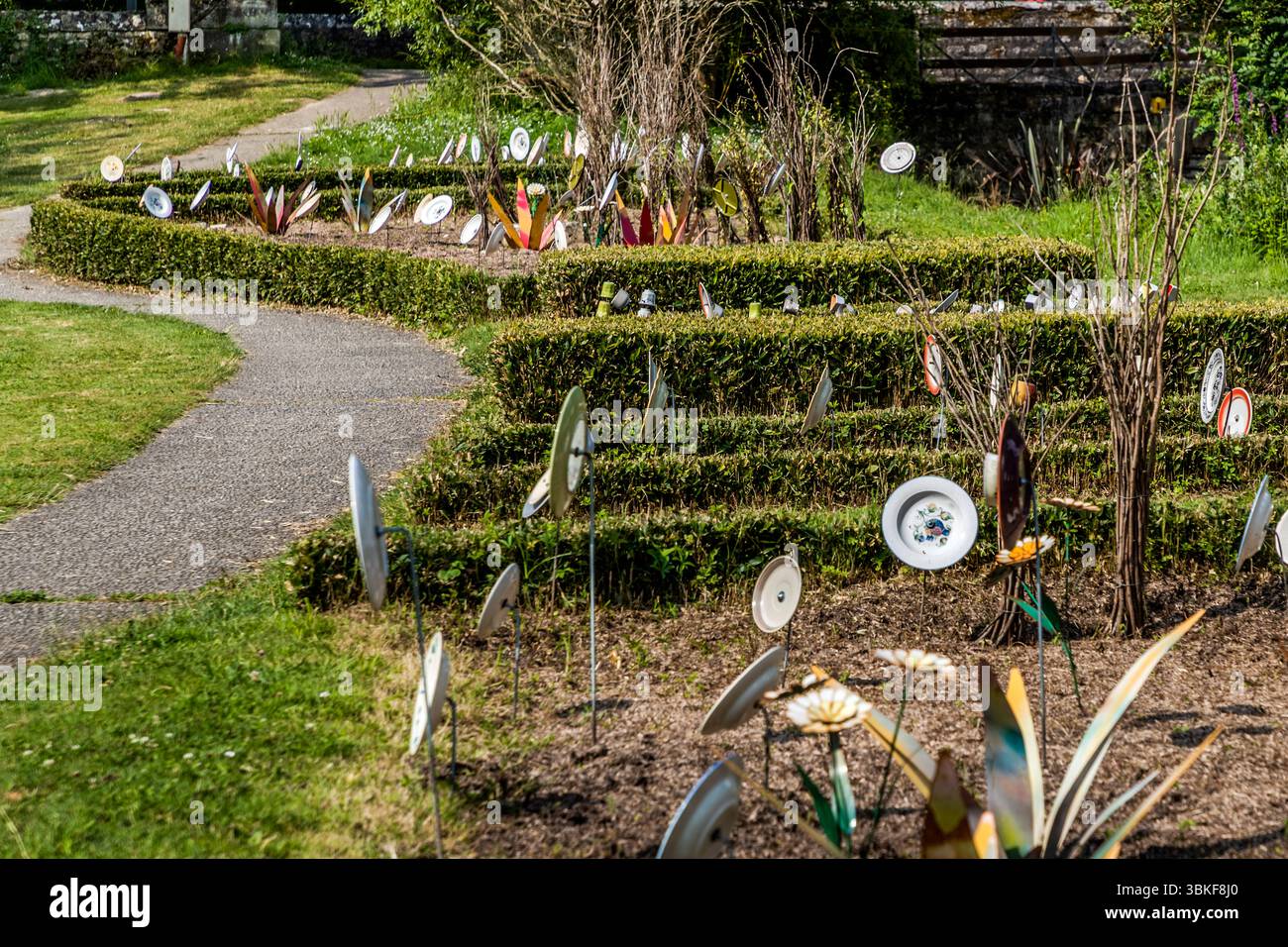 Plaques sur poteaux dans un jardin avant en France, Nouvelle-Aquitaine. Le motif correspond au proverbe allemand 'Über den Tellerrand schauen' (regardez au-delà du bord de votre assiette), qui fait référence à une attitude ouverte et curieuse dans laquelle on est prêt à transcender ses propres frontières et à apprendre de nouvelles choses. La phrase est souvent utilisée en relation avec le cosmopolitisme, un changement de perspective ou une innovation. Penser hors de la boîte. L'installation décorative de jardin comprend différentes pièces de vaisselle attachées à des bâtons et placées dans un parterre de fleurs pour créer une scène ludique et artistique. L'installation est Banque D'Images