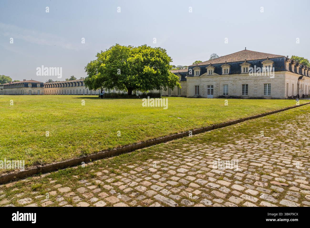 Le complexe de la Corderie Royale à Rochefort, vue du quai Joseph Bellot : pavés, vieux platane et pavillon d'entrée de l'ancien arsenal naval, derrière lequel s'étend l'installation royale de fabrication de cordes de 374 mètres de long. Le complexe a été construit en 1666 sur ordre du ministre d’État Jean-Baptiste Colbert pour approvisionner en corde la marine de Louis XIV. Quai Joseph Bellot, Rochefort, Charente-maritime, Nouvelle-Aquitaine, France Banque D'Images