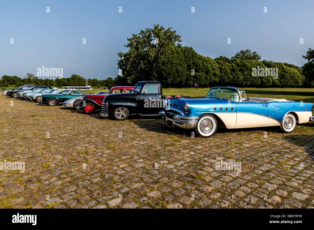 Les voitures classiques se rencontrent dans la rue pavée devant la Corderie Royale à Rochefort : plusieurs voitures américaines des années 1950 et 1960 sont alignées, dont, au premier plan, un cabriolet Buick de milieu de gamme (c. 1955) en bleu et blanc, ainsi qu’un modèle noir Chevrolet du début des années 1950 Quai Joseph Bellot, Rochefort, Charente-maritime, Nouvelle-Aquitaine, France Banque D'Images