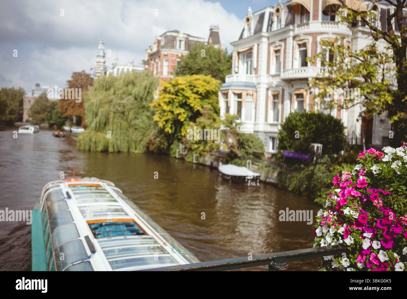 La conception plate représente le toit en verre bateau d'excursion glissant sur l'eau du canal, le planteur en fleurs et la maison de ville Banque D'Images