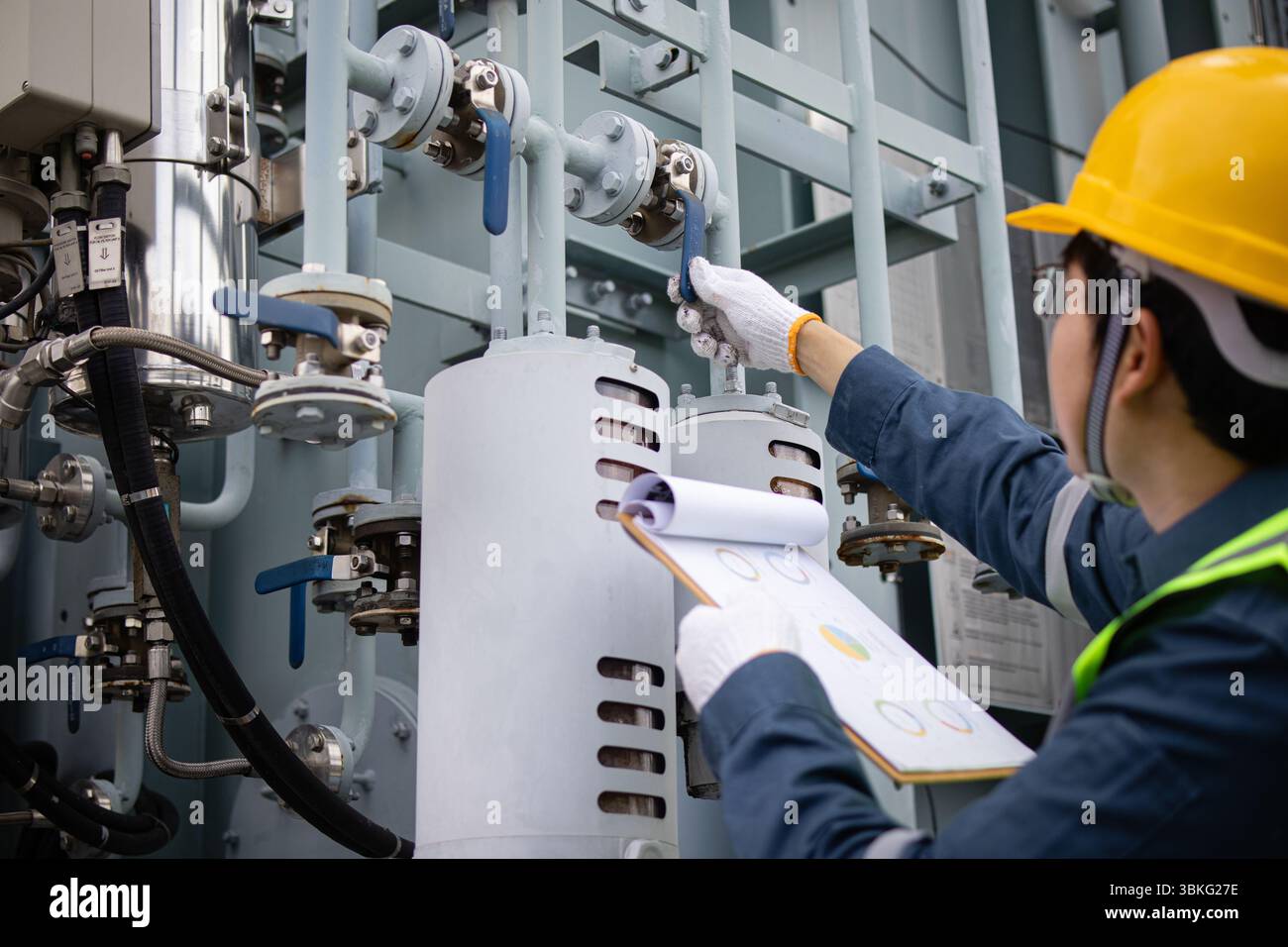 Un ingénieur effectue l'inspection de l'équipement industriel dans les vannes et les tuyaux de contrôle de sous-station tout en tenant une presse-papiers pour assurer le système de transformateur o Banque D'Images