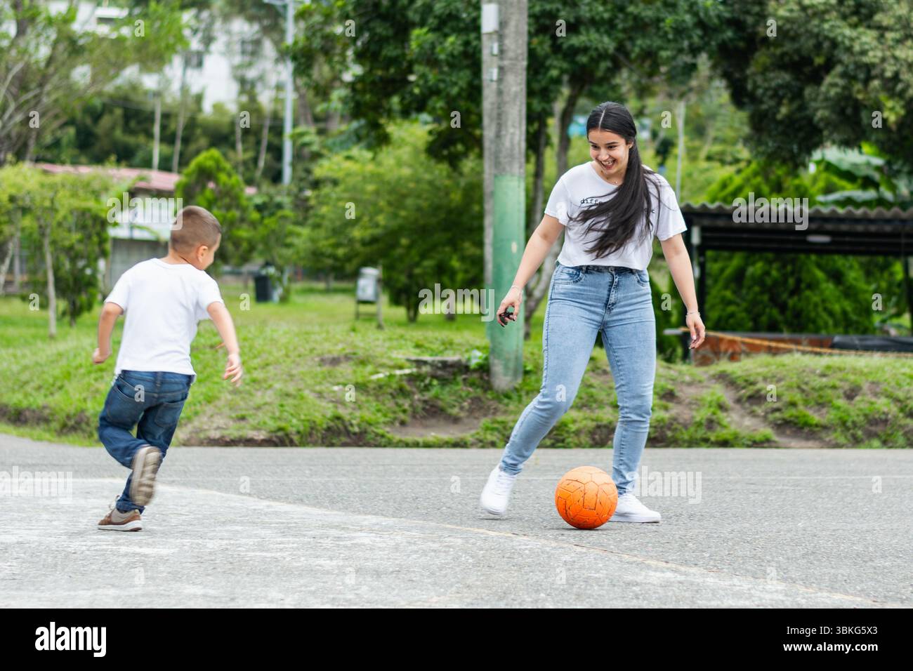 Jeune mère latine et enfant jouant au football dans le parc sur un terrain de ciment avec un ballon de football orange Banque D'Images