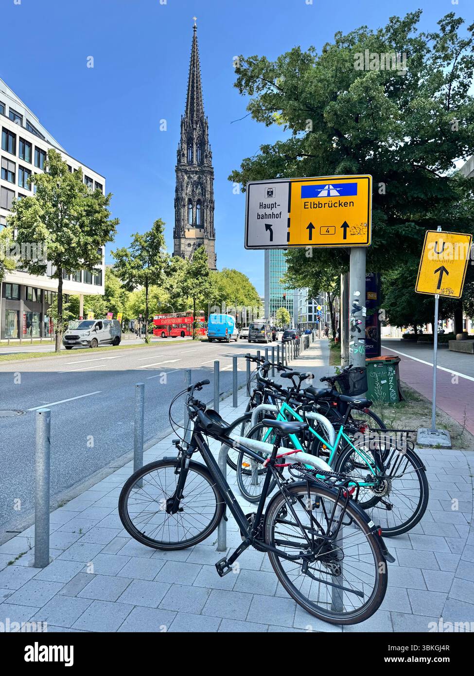 Vélos garés sur une rue ensoleillée avec la flèche de l'église de Nicolas en arrière-plan, Hambourg, Allemagne. Banque D'Images
