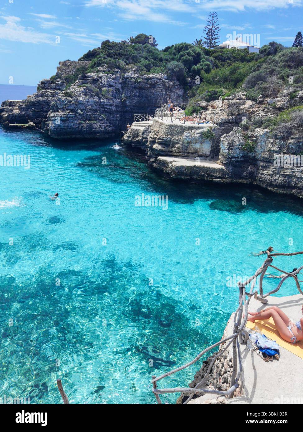 Jambes relaxantes, eau turquoise, ambiance estivale - Une scène paisible de jambes embrassées par le soleil reposant sur le bord de Cala en brut, Minorque. La mer turquoise belo Banque D'Images
