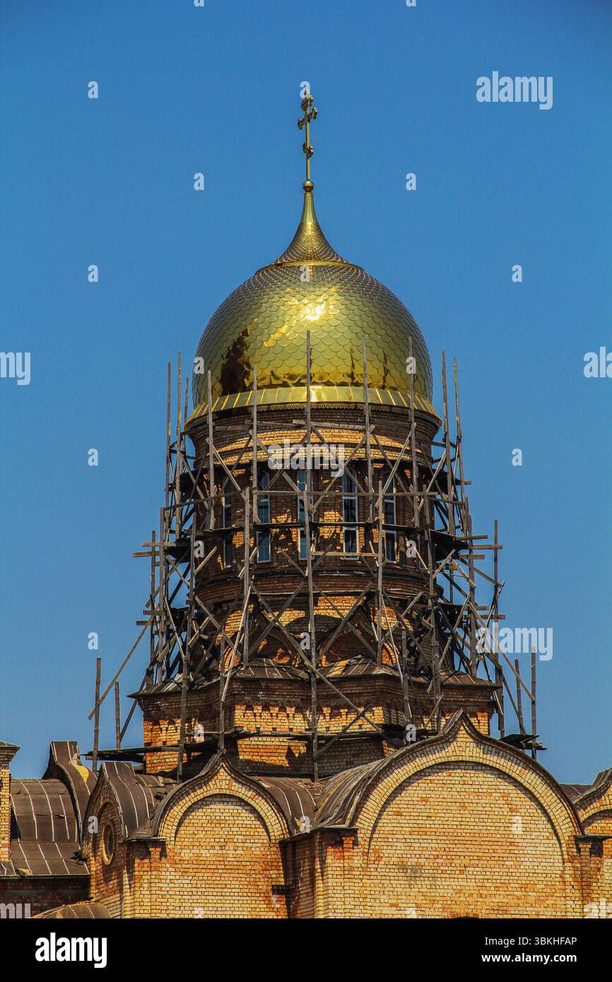 Une vue détaillée d'un dôme doré sur une église orthodoxe en cours de restauration, entouré d'échafaudages en bois contre un ciel bleu clair. Banque D'Images