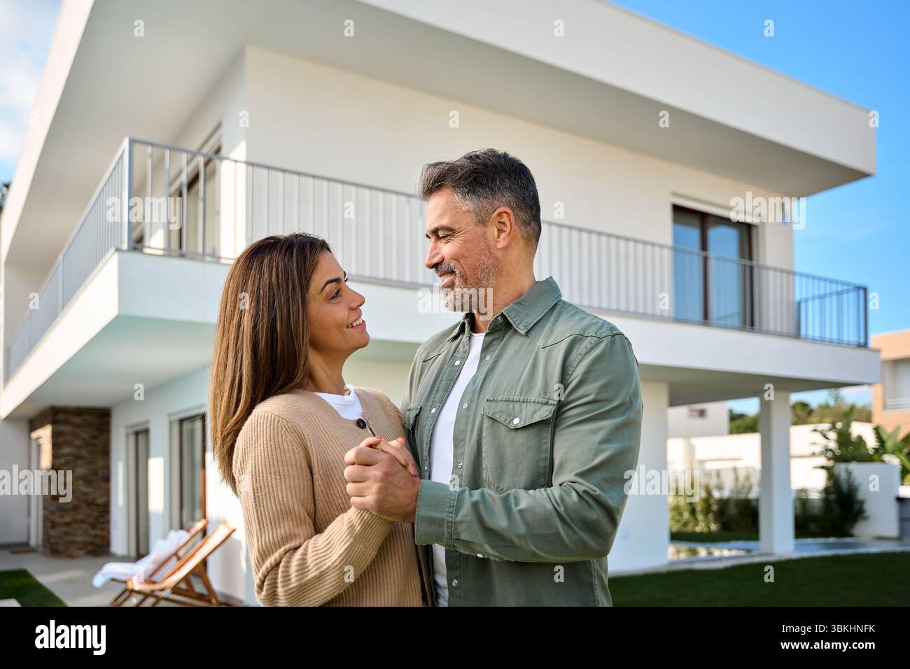 Heureux souriant couple d'âge moyen acheteurs de nouvelles propriétés debout à l'extérieur de la maison. Banque D'Images