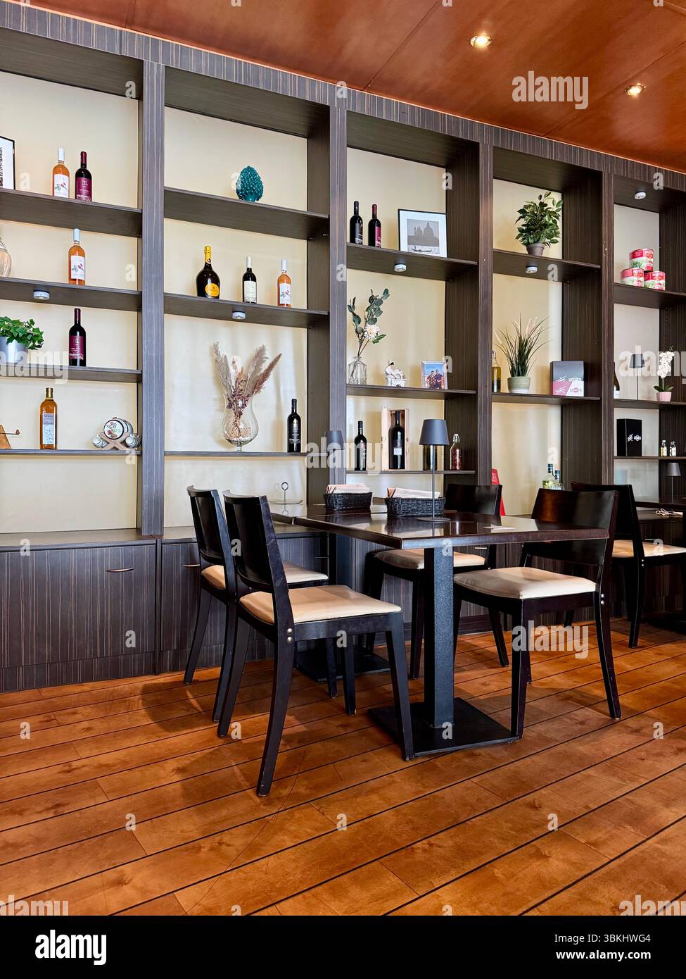 Un intérieur de restaurant élégant en Allemagne, avec des planchers en bois, des étagères en bois sombre avec des objets décoratifs et des bouteilles, et une configuration propre pour la salle à manger. - Image de stock capturée avec un smartphone