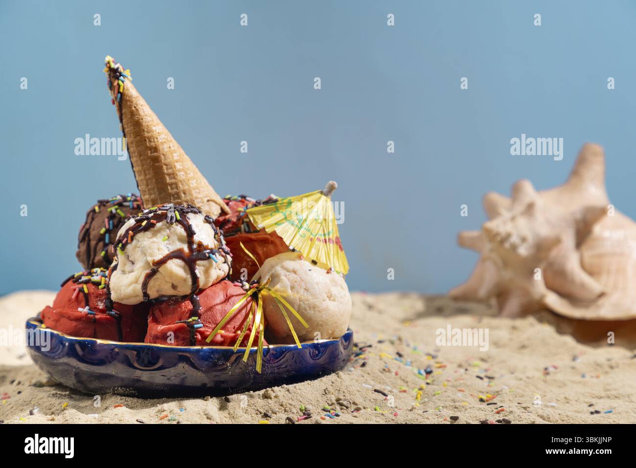Différentes saveurs de crème glacée avec sauce chocolat, crumble et parasol sur sable avec coquillages Banque D'Images