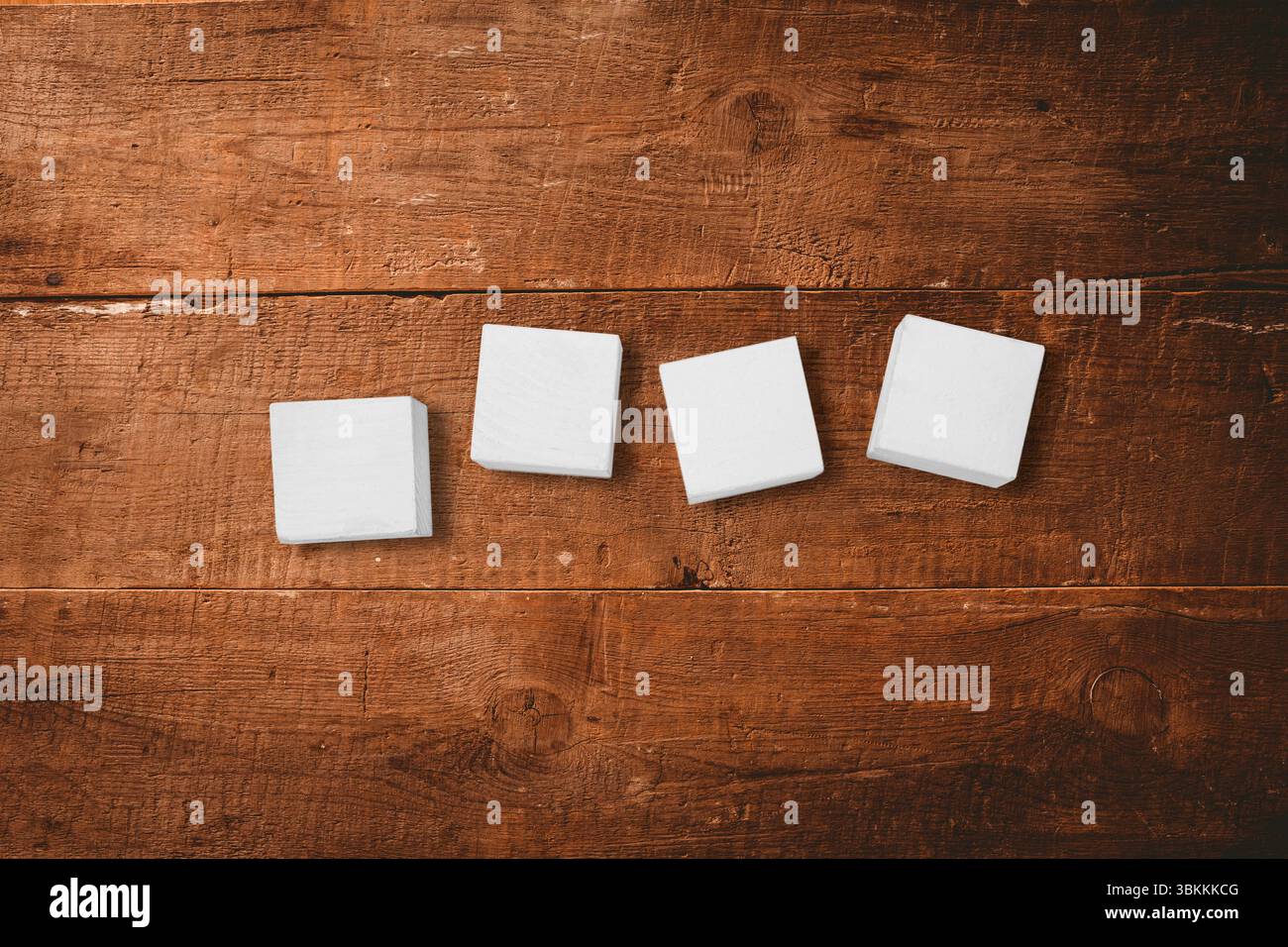 Quatre blocs carrés blancs sont assis uniformément espacés sur une table en bois rustique dans un design plat Banque D'Images