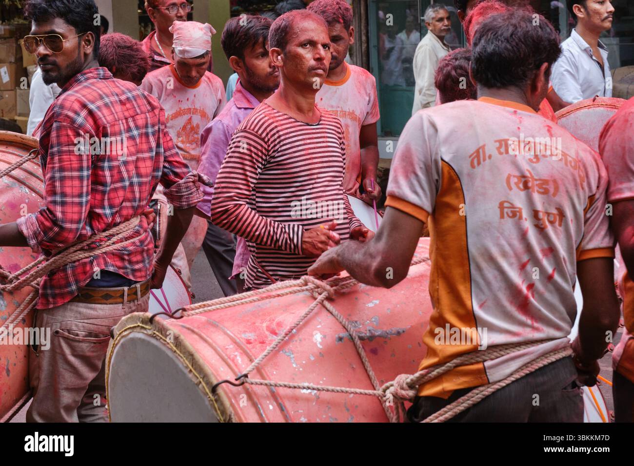 Un groupe de batteurs couverts de poudre de gulal rouge (gulaal), lors d'une procession pendant le Ganesh Chaturthi (Festival de Ganesh) à Mumbai, en Inde Banque D'Images