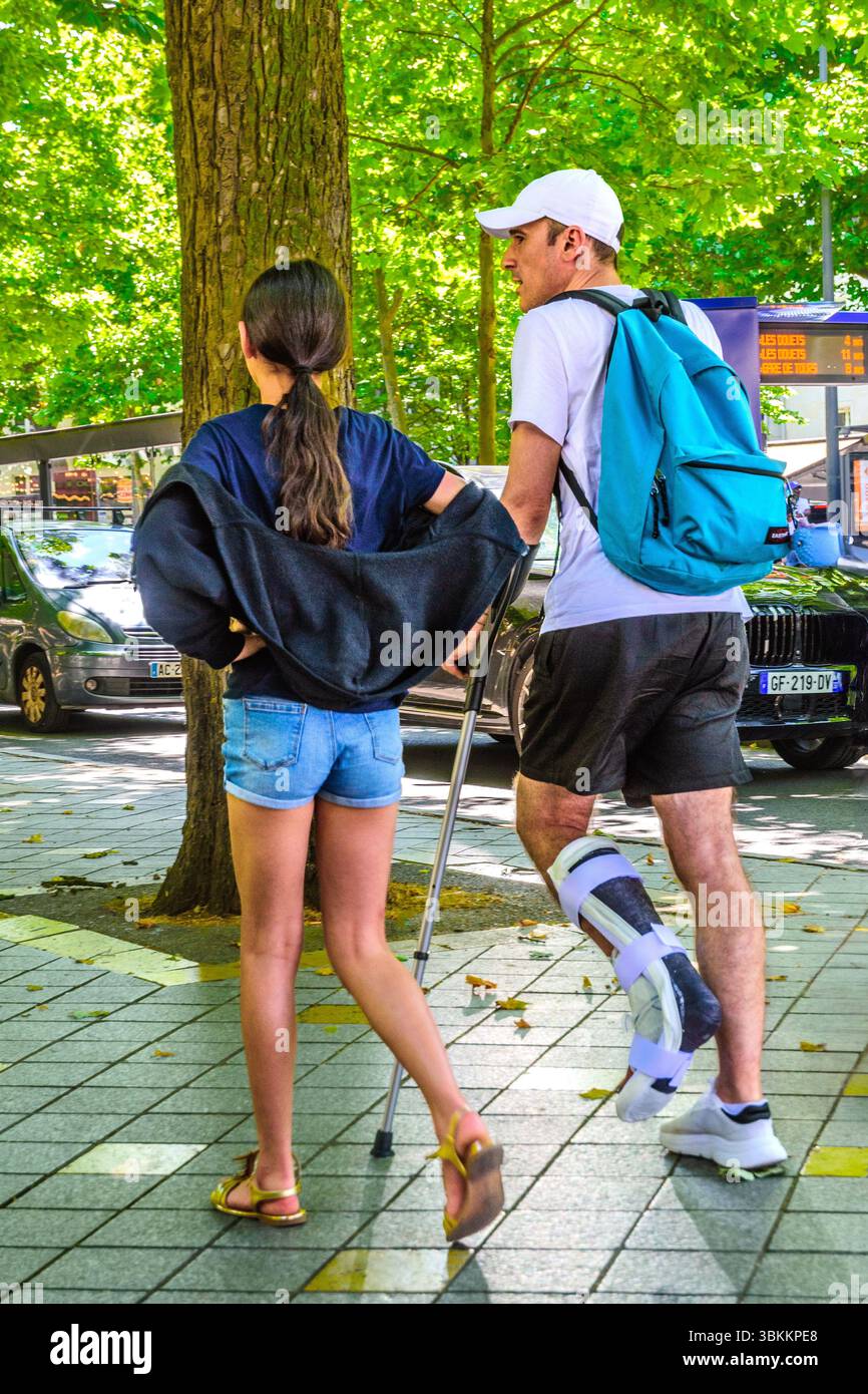 Homme (et jeune fille) avec le pied dans le support en plâtre hospitalier utilisant une aide à la mobilité de bâton de marche réglable - Tours, France. Banque D'Images