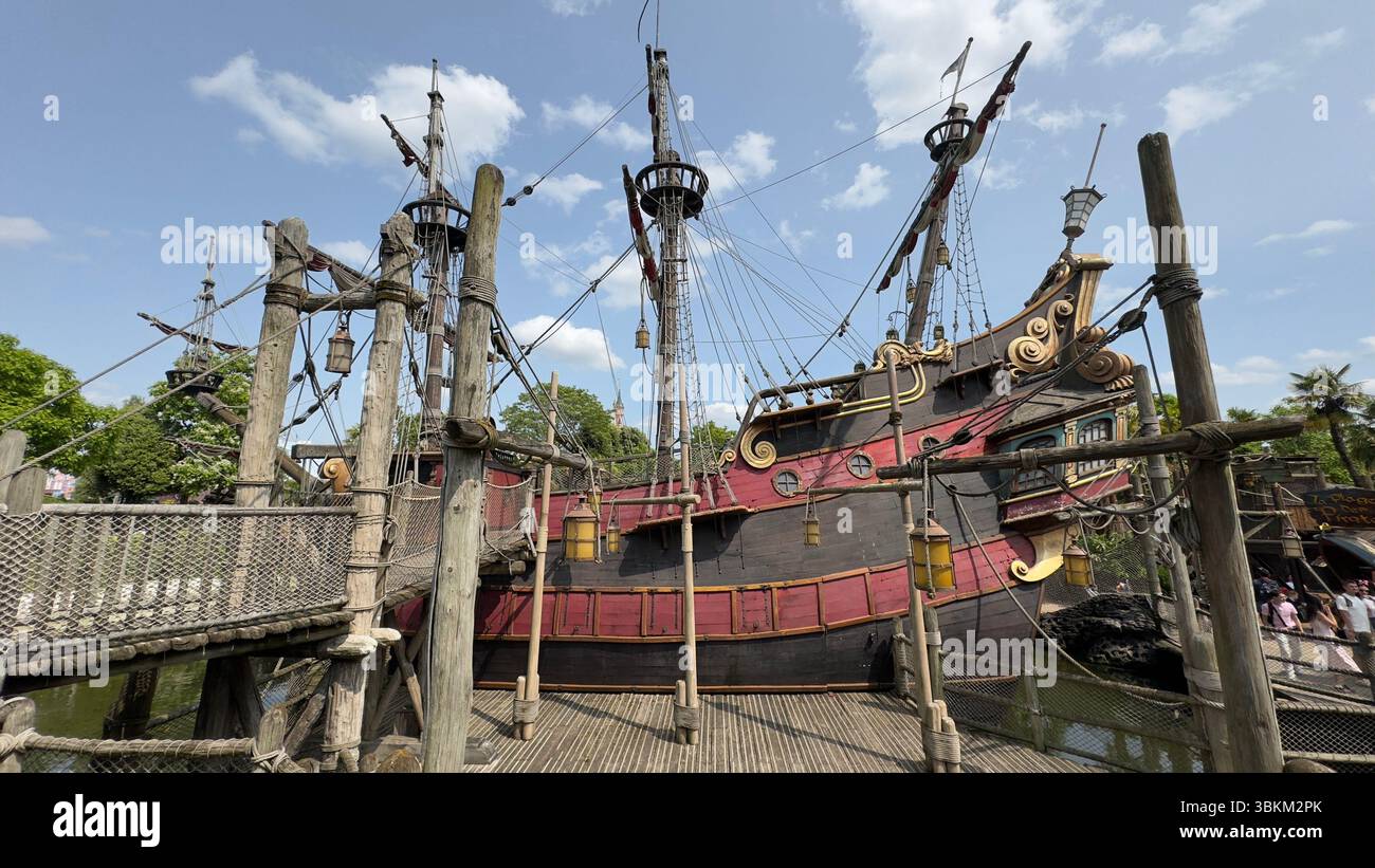 Une réplique de grand bateau pirate domine la scène, reliée par des passerelles en bois au-dessus de l'eau, posée contre un ciel partiellement nuageux. Banque D'Images