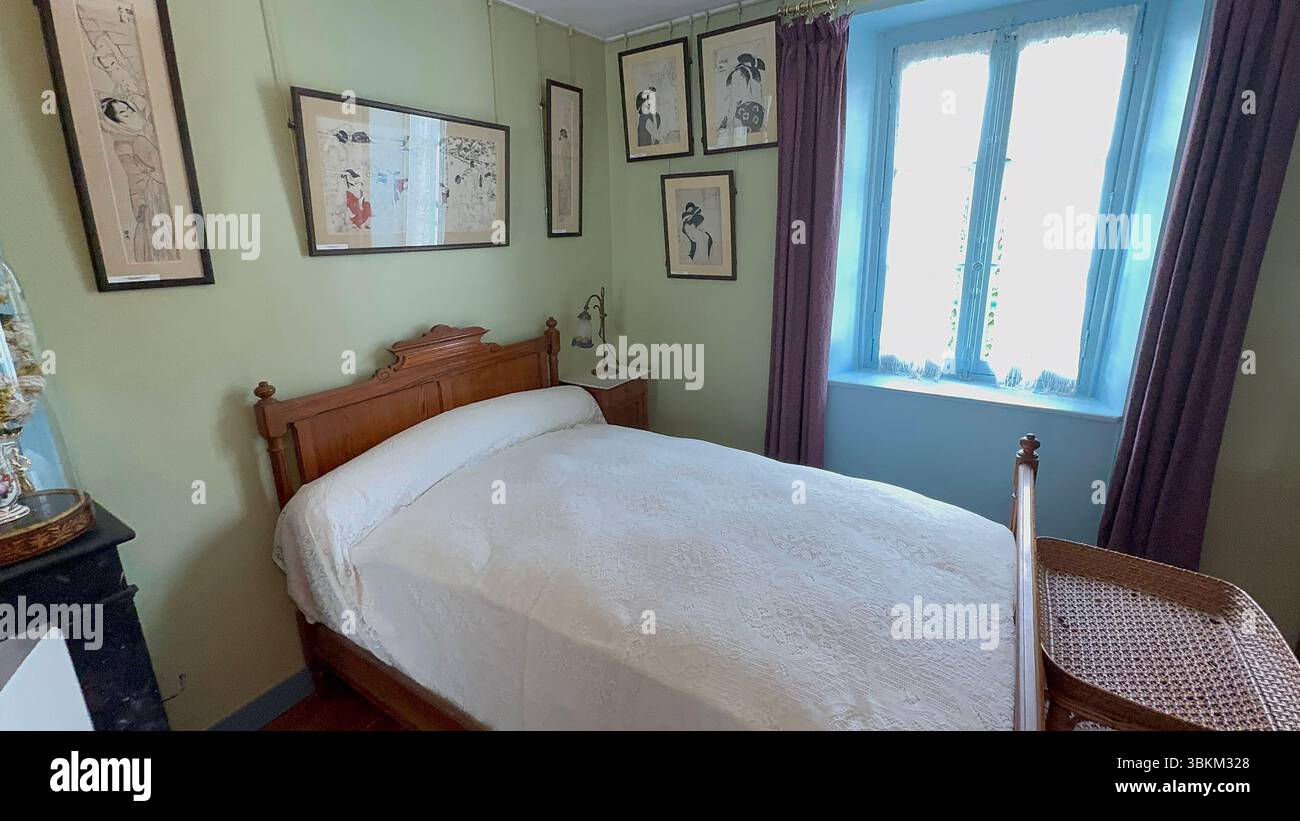 Chambre avec lit en bois, draps blancs et œuvres d'art encadrées sur des murs vert clair. Fenêtre avec cadre bleu et rideaux violets. Banque D'Images