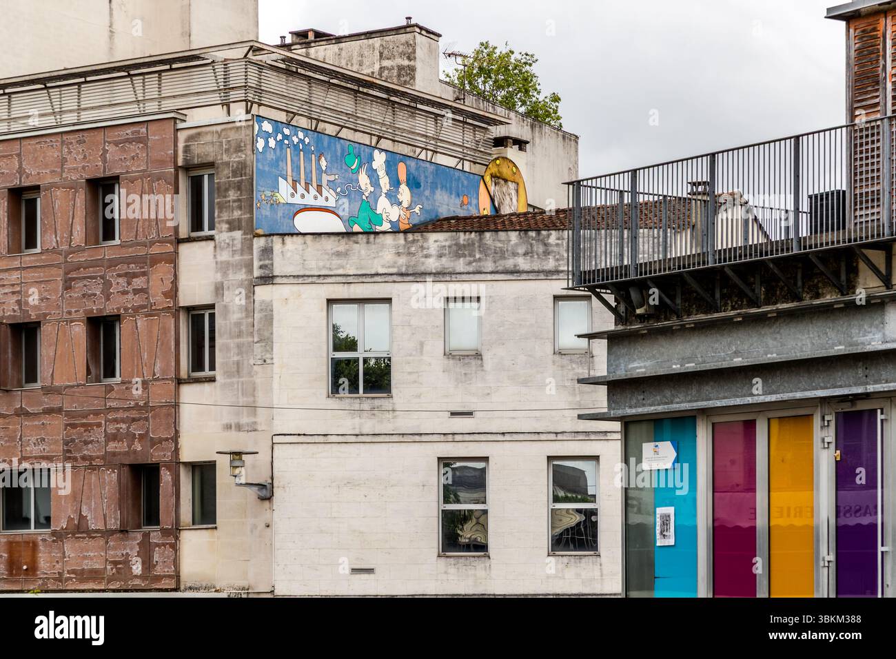 Façades de bâtiments sur la place du champ de mars à Angoulême : sur le toit de l’un des bâtiments, une grande murale représentant des personnages de la tradition comique franco-belge ; des éléments de porte colorés sont visibles sur le bord droit de l’image. Angoulême accueille le Festival International de la bande dessinée, le plus important festival international de la bande dessinée, et intègre la culture de la bande dessinée dans le paysage urbain de bien des façons. Angoulême est reconnue comme ville créative de l’UNESCO dans la catégorie littérature depuis 2019. Place du champ de mars, Angoulême, Charente, Nouvelle-Aquitaine, FR Banque D'Images