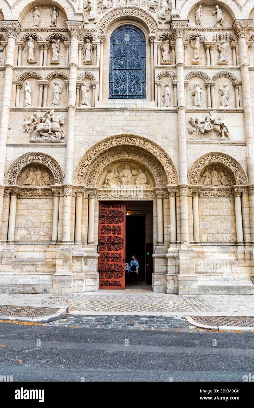 Façade ouest de la cathédrale Saint-Pierre d’Angoulême (XIIe siècle) : les archivoltes à plusieurs niveaux et les niches figuratives du portail principal présentent un décor figuratif roman ; les portes en bois rouge de l’entrée principale sont ouvertes et une personne quitte le bâtiment. La cathédrale est classée « Monument historique » et fait partie de la voie de St James (via Turonensis). Place Saint-Pierre, Angoulême, Nouvelle-Aquitaine, France Banque D'Images