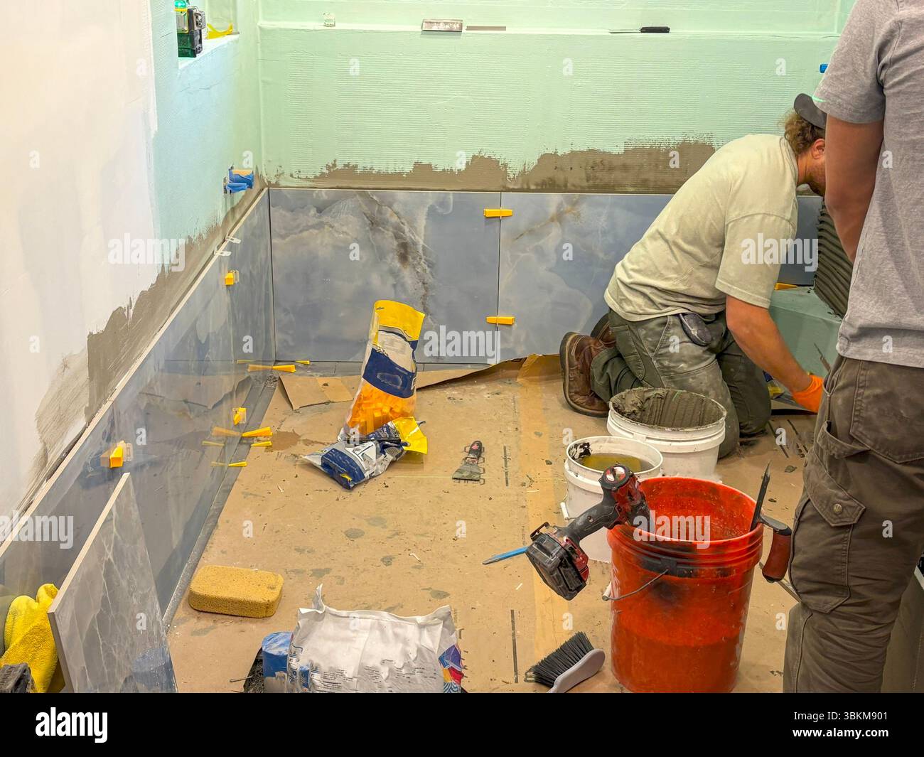 Les travailleurs sont occupés à carreler un mur de salle de bains pendant les travaux de rénovation en cours. Banque D'Images
