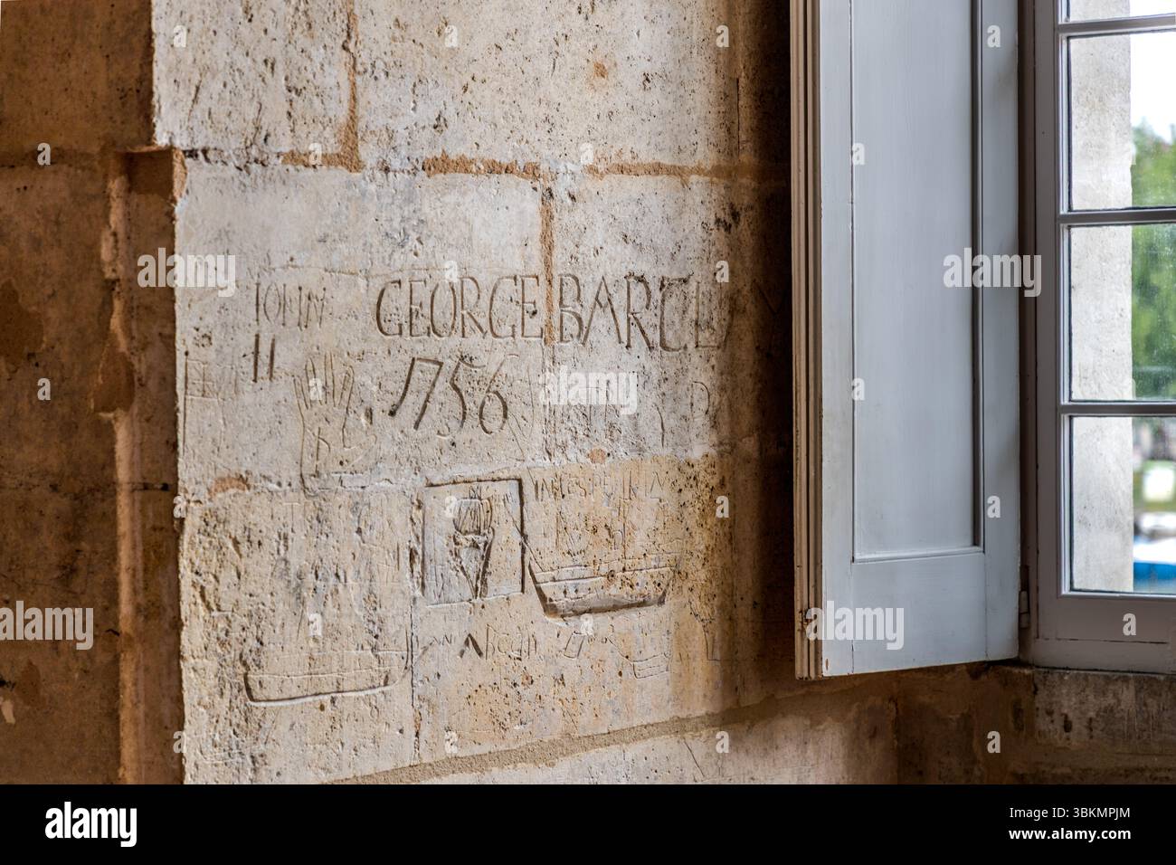 Des gravures sur pierre recouvrent un mur à côté d'une fenêtre du château de Cognac, Rampe du Château, Cognac, Nouvelle-Aquitaine, France. Gravés dans la pierre figurent le nom « John George Barclay » et l'année 1756. En dessous se trouvent le contour d'une main, un blason et des navires à voile gravés dans le calcaire. Pendant la guerre de Sept Ans, le château a servi de prison pour les captifs étrangers, qui ont laissé des graffitis sur ses murs. L'inscription a probablement été faite par un prisonnier de guerre anglais. Banque D'Images