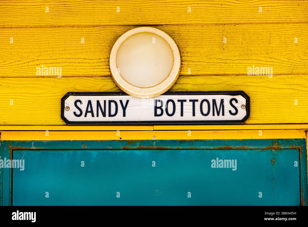 Un mur de cabane de plage en bois jaune vif est orné d'une lumière circulaire et d'un panneau indiquant « FOND DE SABLE » au-dessus d'une porte sarcelle seaton carew co. durham uk Banque D'Images