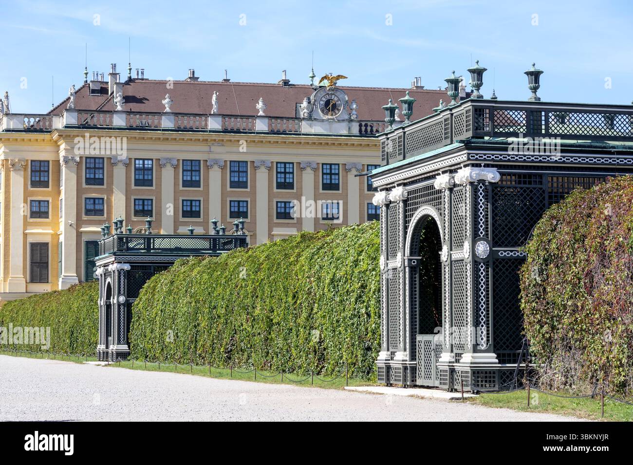 Un complexe de palais avec un bâtiment baroque jaune à l'arrière-plan, des murs de haies verts, clipsés, et une porte sombre et décorative ou un élément structurel en th Banque D'Images