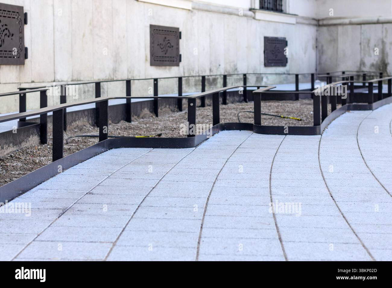 un système moderne de passerelle en pavé gris avec des bordures en métal noir et des garde-corps qui longe un mur blanc de bâtiment avec des fenêtres décoratives. Banque D'Images