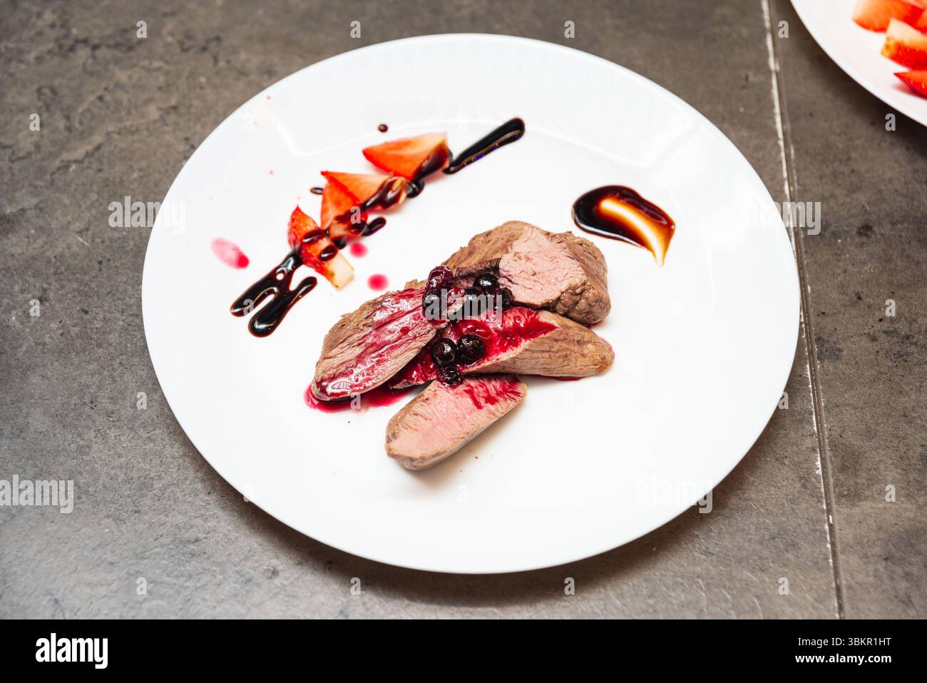 Présentation gourmande de filet de venaison tendre servi avec réduction de baies et garniture de fraise sur une assiette blanche. Banque D'Images