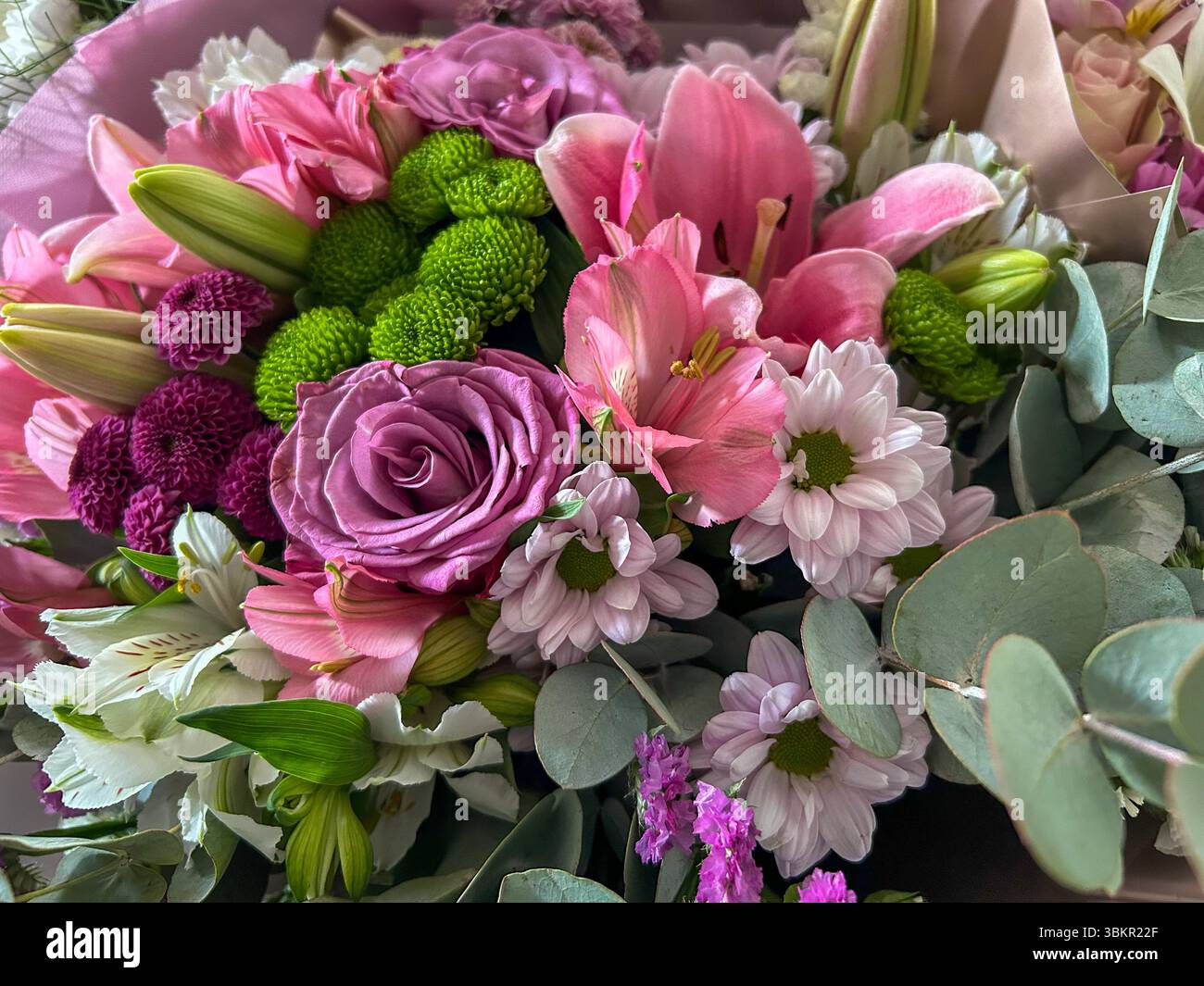 Vue détaillée d'un bouquet vibrant avec des lis roses, des roses violettes, des chrysanthèmes verts, des marguerites et des feuilles d'eucalyptus, parfait pour un motif floral - Image de stock capturée avec un smartphone