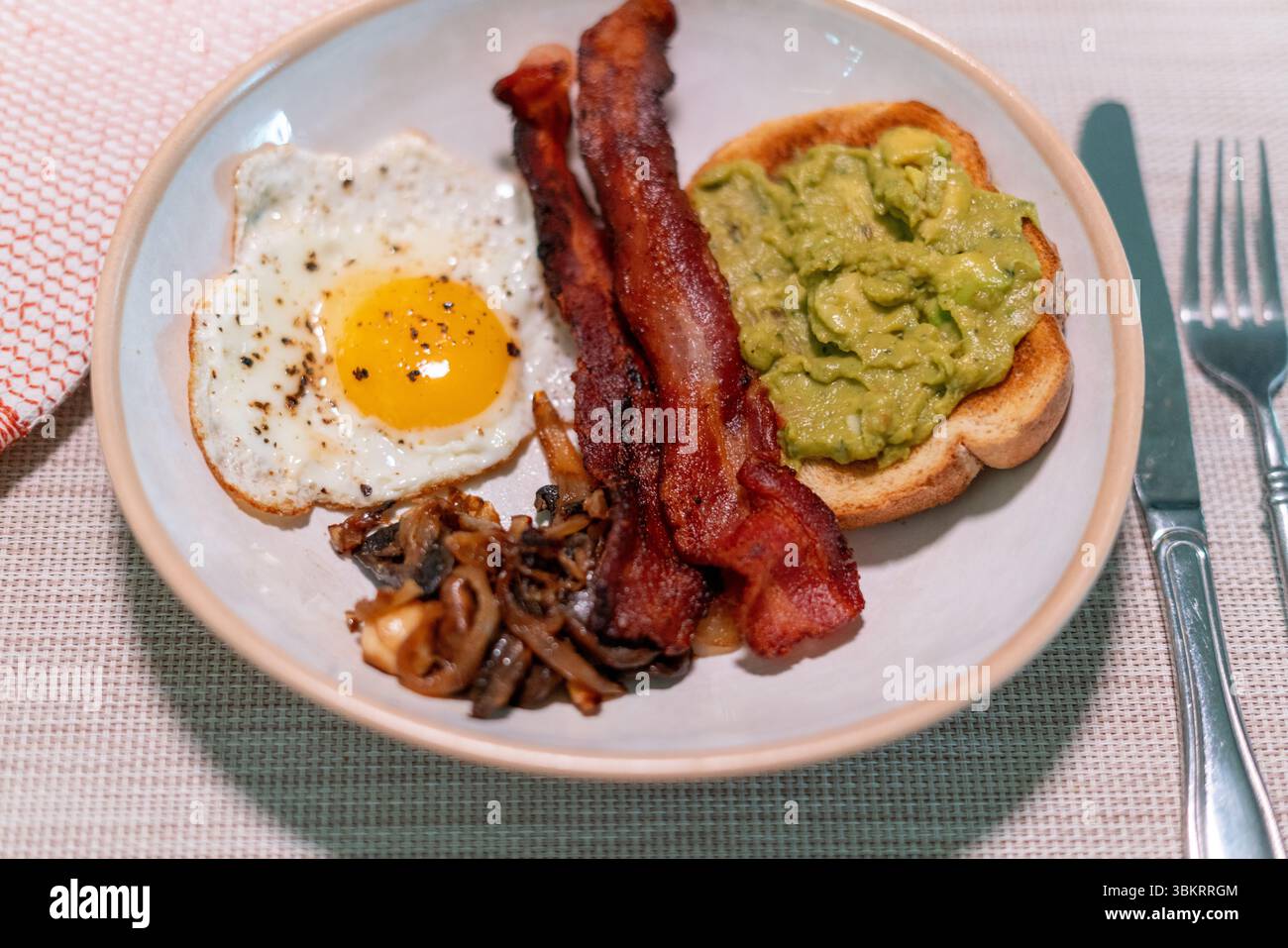 Copieux petit déjeuner avec bacon croustillant, œuf au plat, champignons sautés et pain grillé crémeux à l'avocat sur un plat rustique en céramique, parfait pour les menus du brunch. Banque D'Images