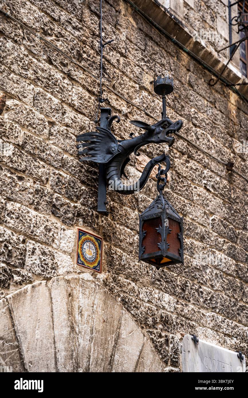 Lanterne décorative en fer forgé en forme de dragon sur un mur de pierre dans le centre historique médiéval d'assise, Ombrie, Italie Banque D'Images