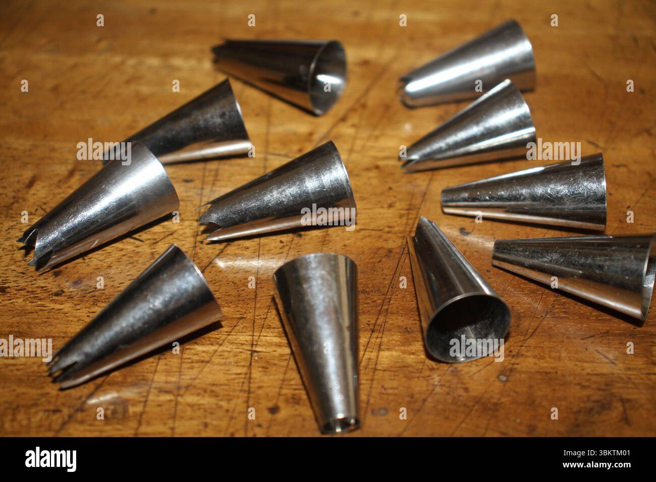 Collection de pointes de tuyauterie métalliques disposées en cercle sur une surface en bois. Ces pointes coniques, couramment utilisées dans la décoration de gâteaux. Banque D'Images