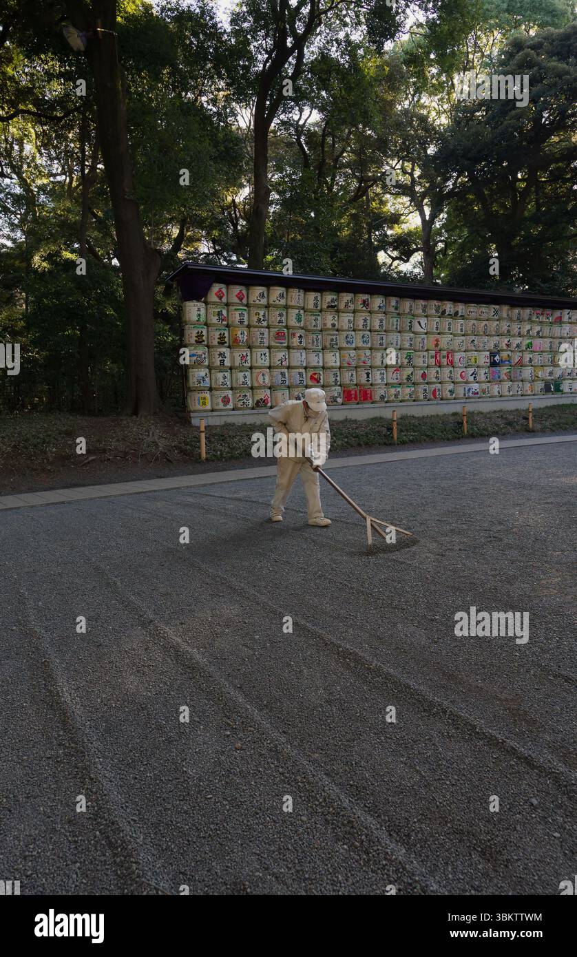 Gardien de sol ratissant méticuleusement les chemins de gravier au sanctuaire Meiji Jingu à Tokyo Banque D'Images