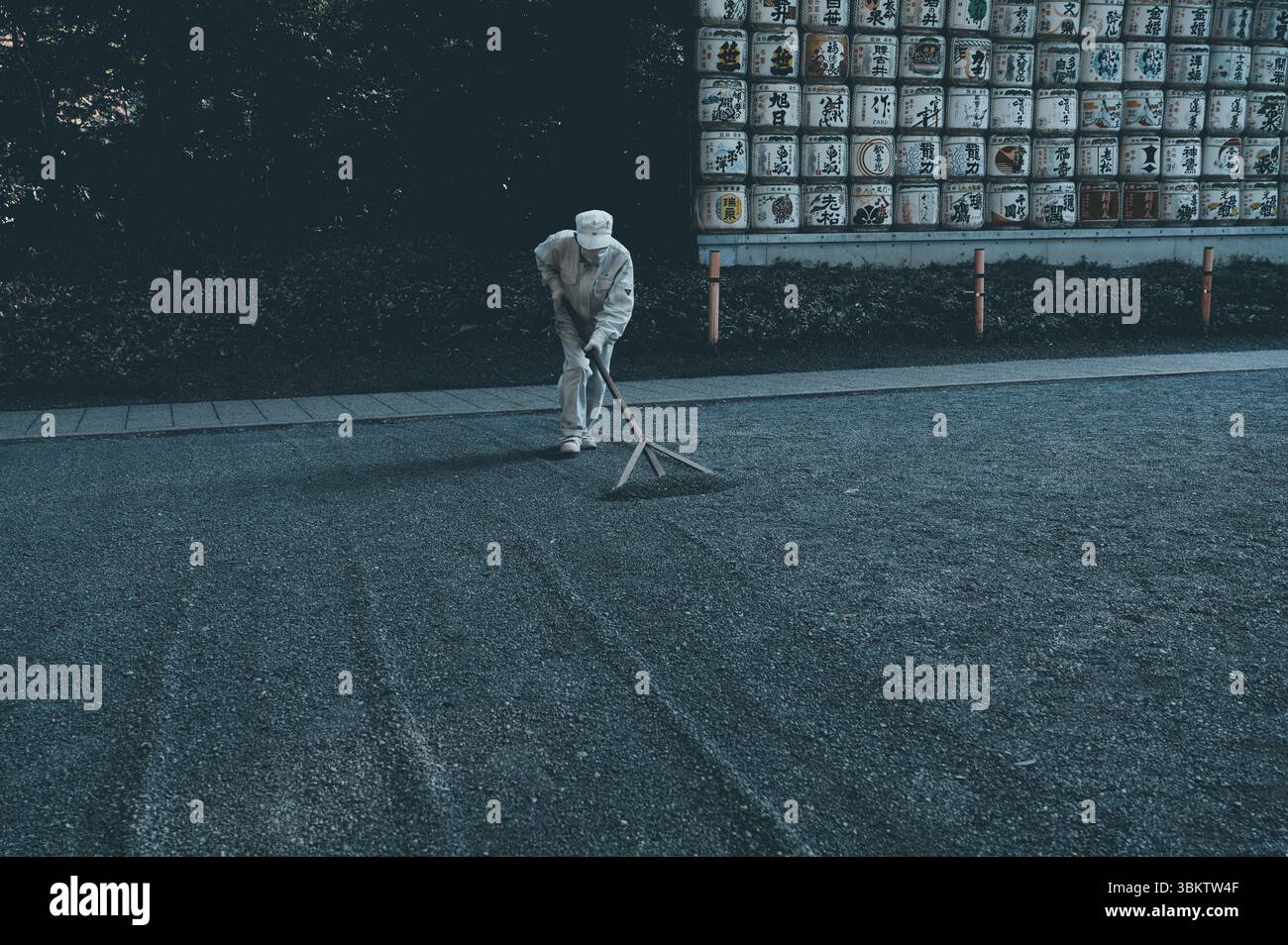Un ouvrier du sanctuaire râle méticuleusement le chemin de gravier du sanctuaire Meiji Jingu Banque D'Images