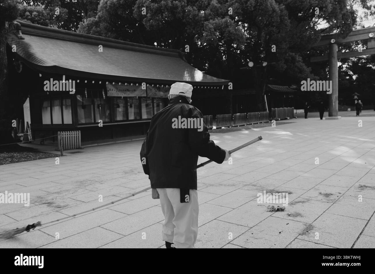 Un gardien du sanctuaire balaie tranquillement le chemin de pierre du sanctuaire Meiji Jingu Banque D'Images