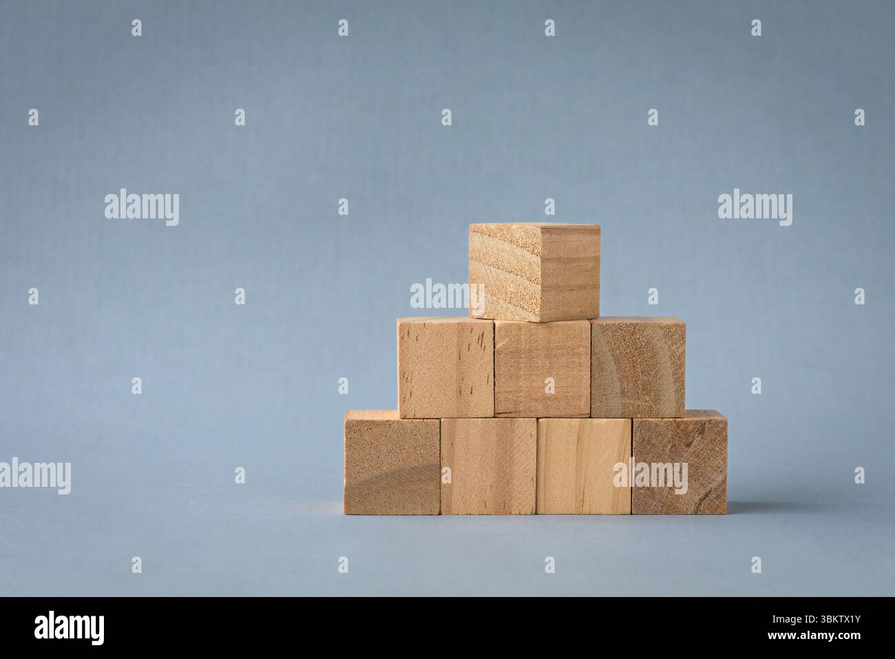 Blocs carrés en bois disposés en forme de pyramide. Isolé sur fond clair, espace de copie. Banque D'Images