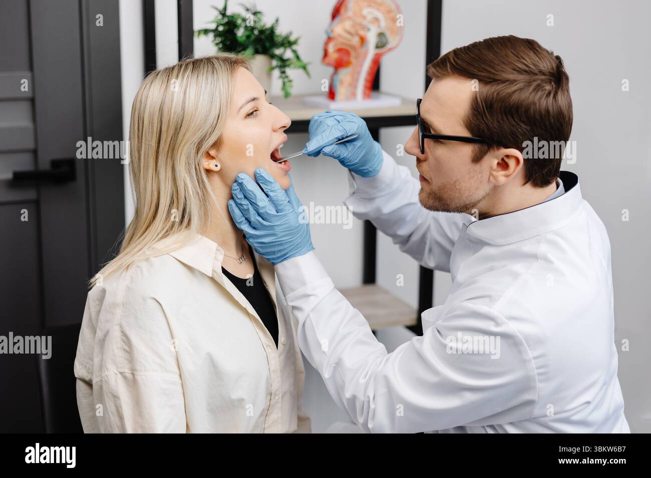 Médecin utilisant une spatule d'inspection pour examiner la gorge du patient. ORL médecin faisant l'examen de gorge d'une femme. La patiente a ouvert la bouche jusqu'à la gorge. Banque D'Images