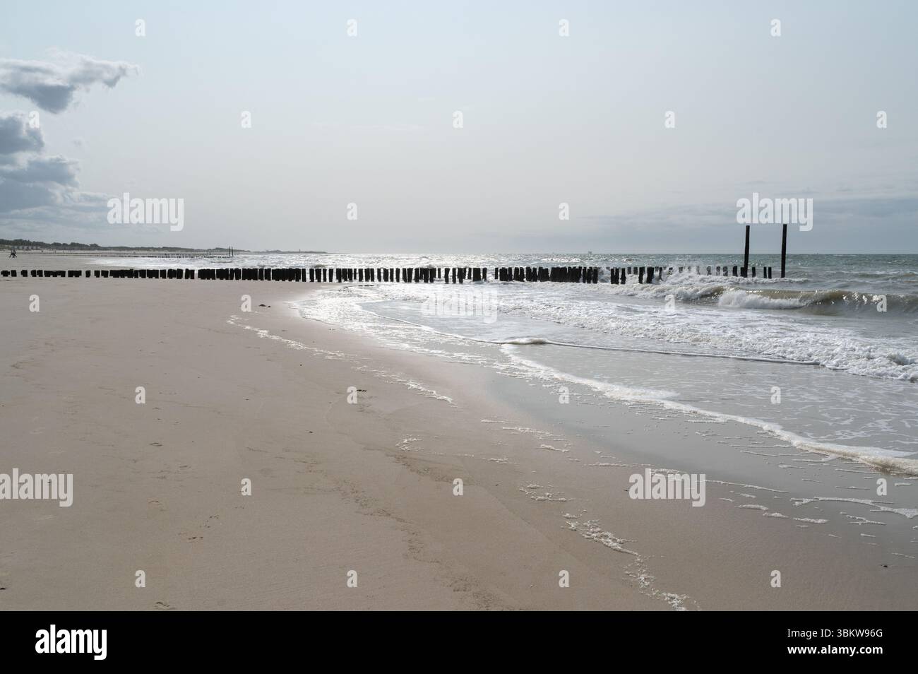 Une vue sereine sur la plage avec de douces vagues le long du rivage et des jetées lointaines sous un ciel nuageux au-dessus Banque D'Images