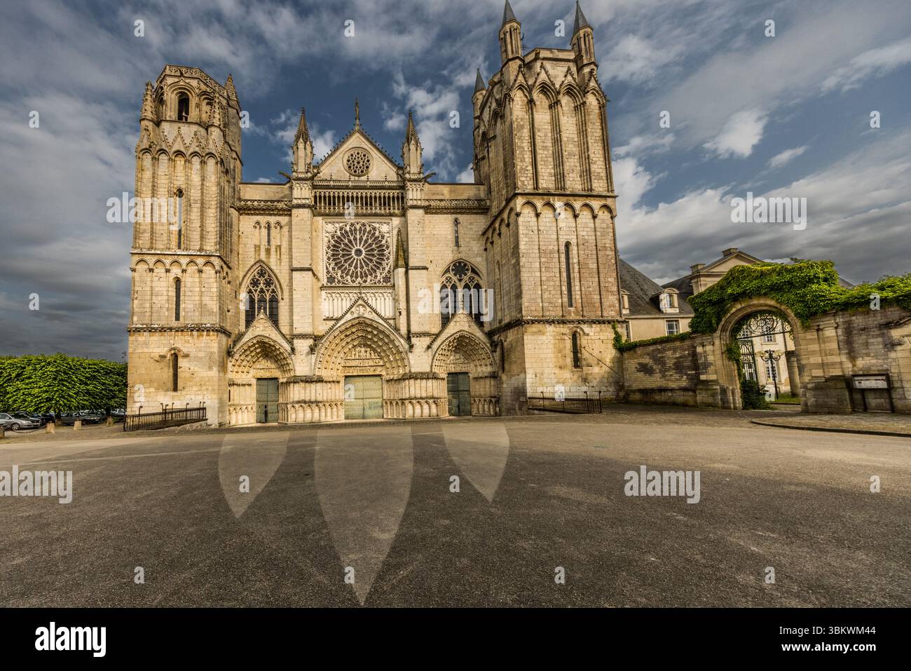 La façade ouest de la cathédrale Saint-Pierre (Cathédrale Saint-Pierre de Poitiers) s'élève sur la Place de la Cathédrale à Poitiers, en Nouvelle-Aquitaine, France. Deux tours inégales encadrent la façade avec ses trois portails et sa grande rosace. À droite, une porte couverte de lierre mène à une cour intérieure. La construction a commencé en 1166 à l'initiative d'Éléonore d'Aquitaine et d'Henri II Plantagenêt. À l'époque, ils étaient roi et reine d'Angleterre ainsi que ducs de Normandie et d'Aquitaine. Ils étaient d'importants mécènes des arts et de la culture de leur temps. Entre autres, ils ont offert les célèbres vitraux Banque D'Images