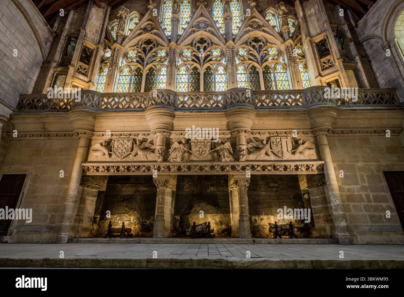Trois cheminées monumentales et richement décorées dominent le mur de fond de la Salle des Pas Perdus (Hall of Lost Steps) dans le Palais des ducs d'Aquitaine sur la Rue Gambetta à Poitiers, en Nouvelle-Aquitaine, France. Des chenets en fer se dressent dans les cheminées. Sur le frise au-dessus, des anges tiennent des armoiries avec des fleurs de lis. Au-dessus d'une galerie en pierre avec une balustrade ajourée s'élèvent trois pignons avec de hautes fenêtres à tracerie en verre coloré. La Salle des Pas Perdus est l'une des plus grandes salles profanes médiévales d'Europe. Le palais, également connu sous le nom de Château de Poitiers, a été f Banque D'Images