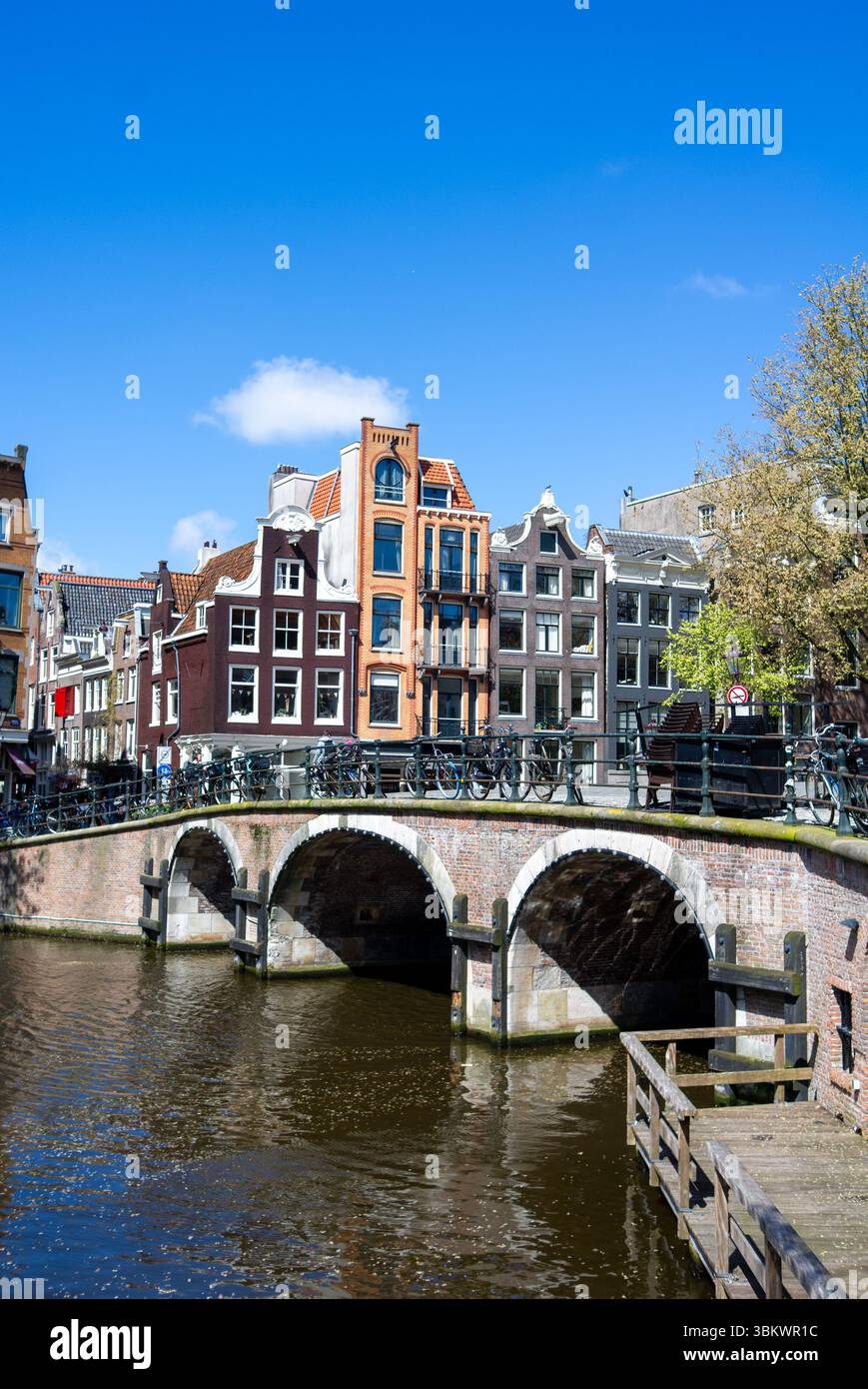 Les gens traversent un pont sur un canal d'Amsterdam, entouré de bâtiments hollandais classiques et de vélos. Banque D'Images