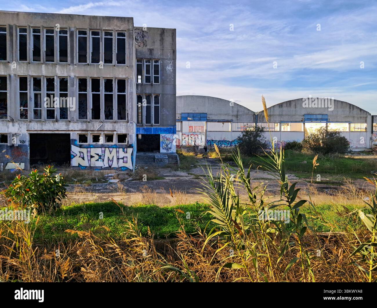 Complexe industriel délabré avec graffitis et végétation envahie, symbolisant la décomposition urbaine et l'abandon Banque D'Images