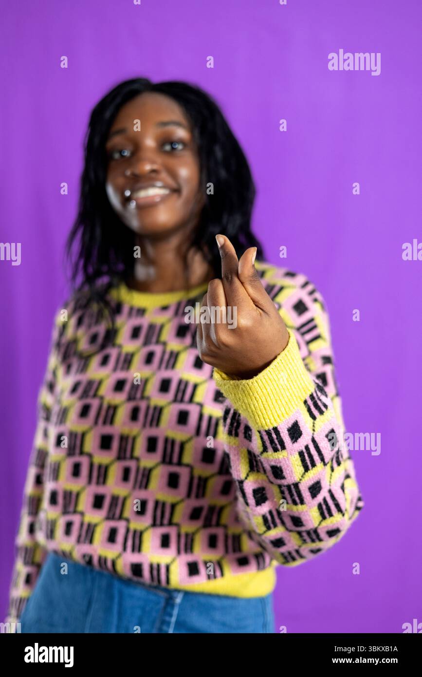 Portrait en studio d'une jeune femme adulte faisant une forme de coeur avec ses doigts, souriant hors foyer en arrière-plan. Elle porte un motif funky Banque D'Images