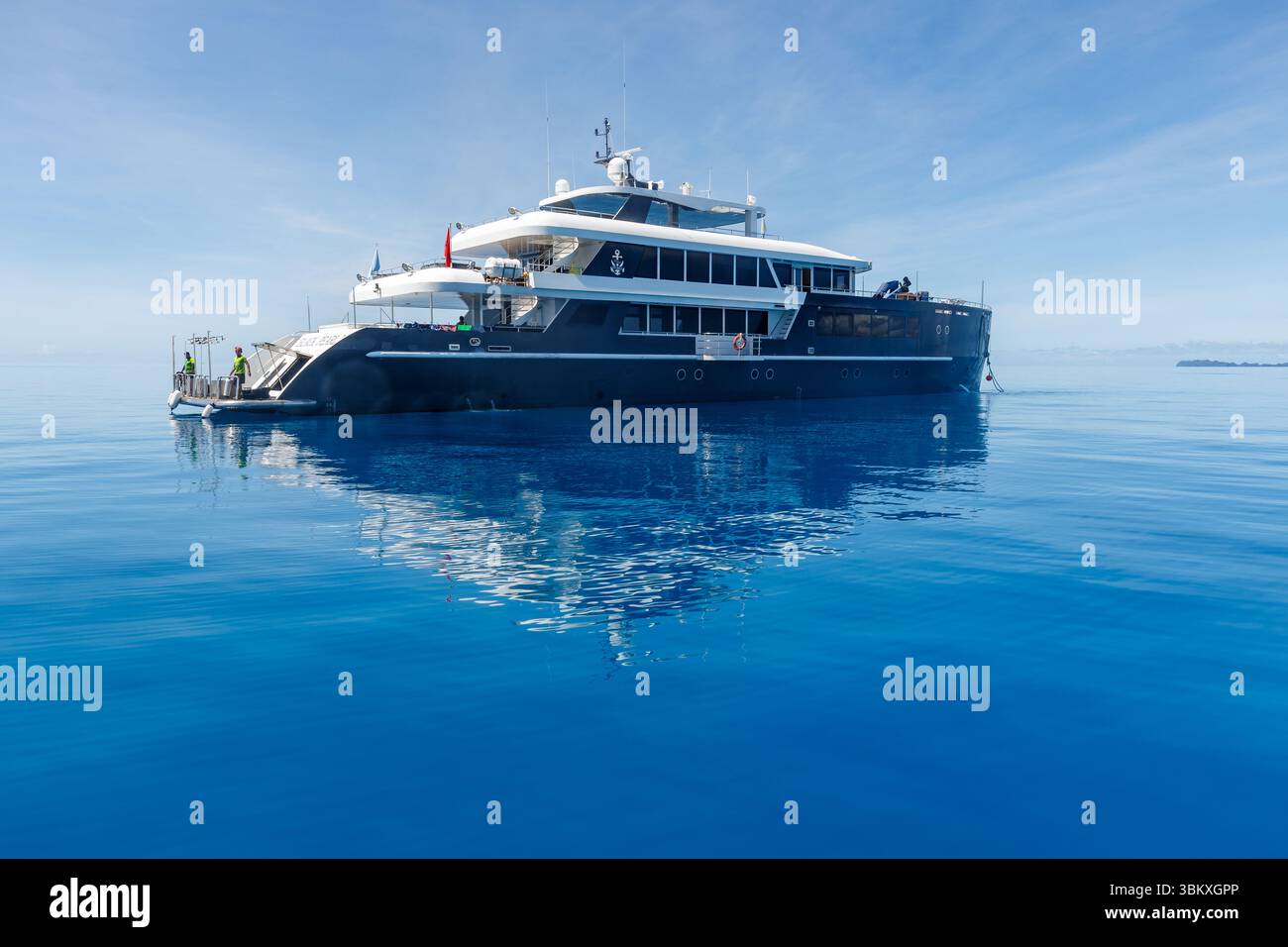 Deux membres d'équipage se tiennent à l'arrière d'un grand yacht, préparant éventuellement le départ ou l'arrivée, par une journée calme et claire. Banque D'Images Deux membres d'équipage se tiennent à l'arrière d'un grand yacht, préparant éventuellement le départ ou l'arrivée, par une journée calme et claire. Banque D'Images