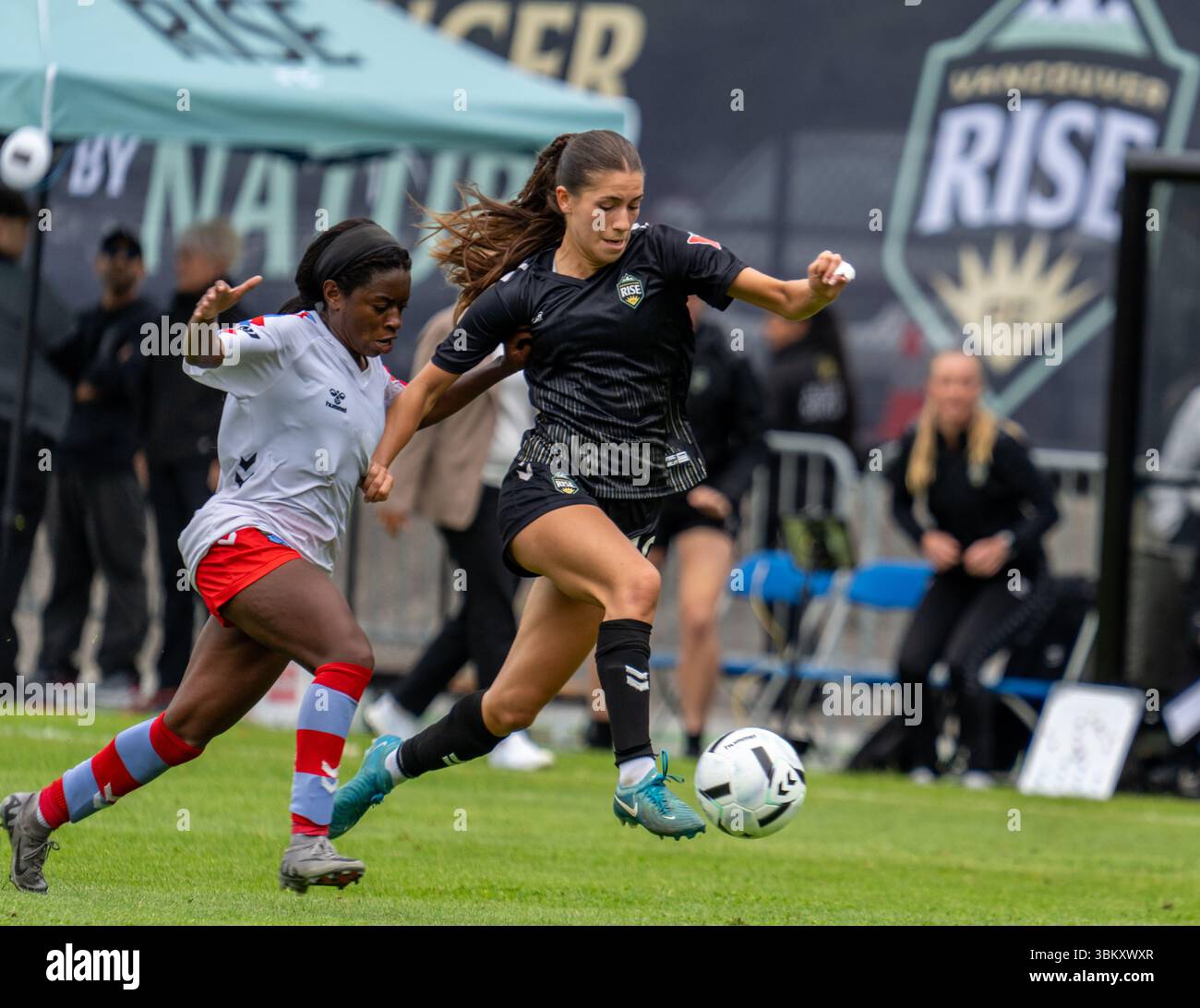 BURNABY, CANADA – 23 JUIN 2025 : Holly Ward, milieu de terrain du Vancouver Rise FC (#19, maillot noir) dribble le ballon en plein champ sous la pression d’un défenseur du Montreal Roses FC lors d’un match de Super League du Nord (NSL). L'action dynamique souligne le rythme rapide du jeu dans la nouvelle ligue de soccer féminine professionnelle du Canada. Crédit : Joe Ng/Alamy Live News Banque D'Images