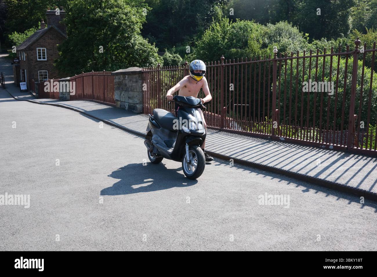 Le premier pont de fer au monde à Ironbridge, Shropshire fermé aux véhicules à moteur il y a plus de 90 ans donc ce jeune garçon pousse le scooter à moteur au-dessus du monument historique. Banque D'Images