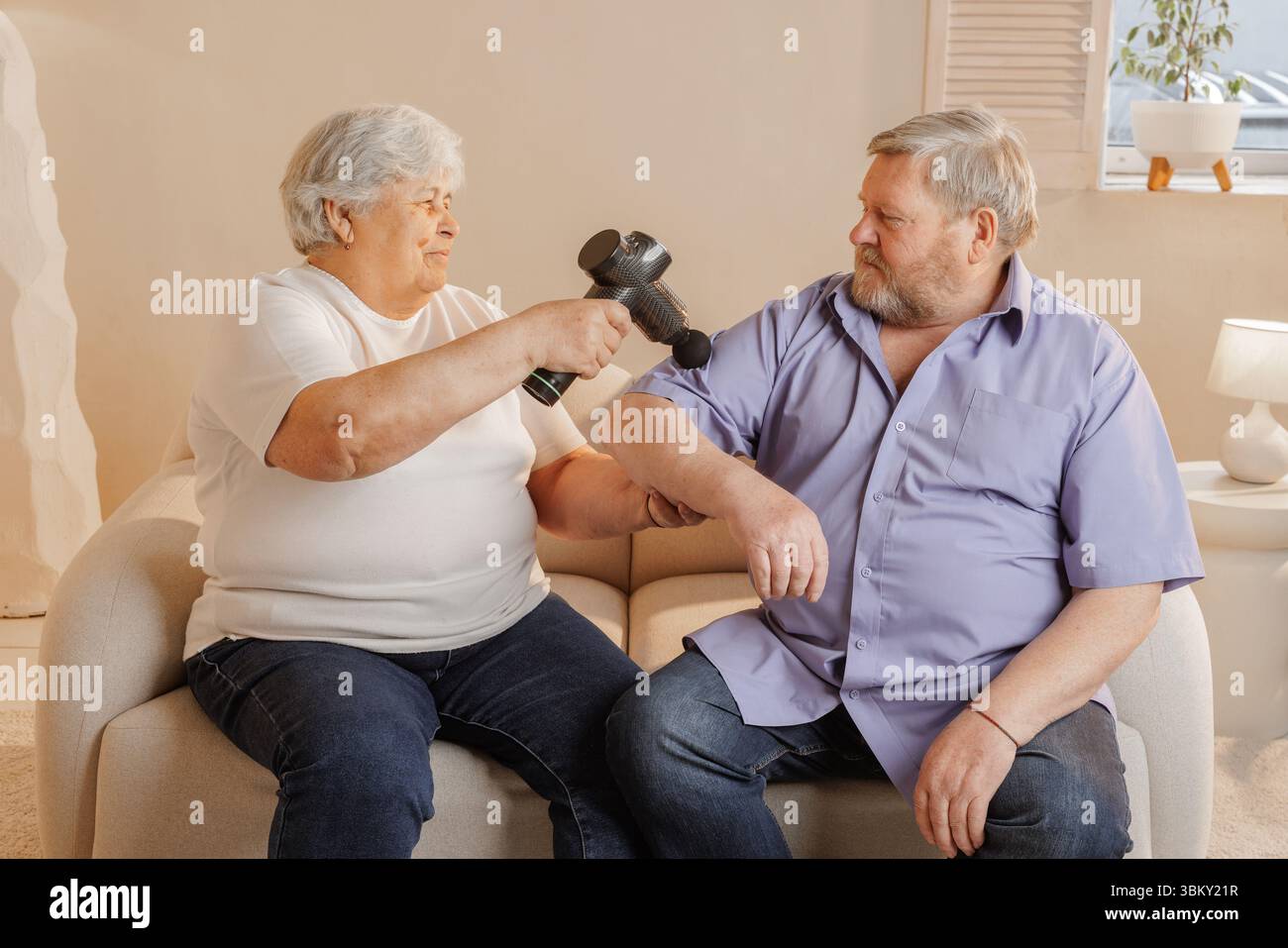 Couple de personnes âgées utilisant un masseur électrique à main à la maison pour soulager la douleur bien-être récupération musculaire et routine de thérapie de soutien Banque D'Images