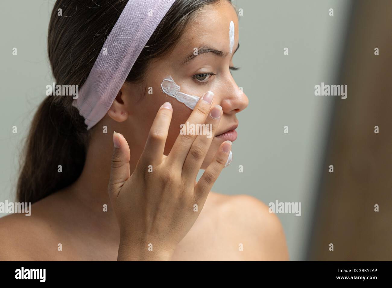 Une jeune femme de profil appliquant une crème cosmétique sur son visage. Un gros plan intime d'une routine quotidienne de soin de la peau et d'un rituel d'auto-soin Banque D'Images