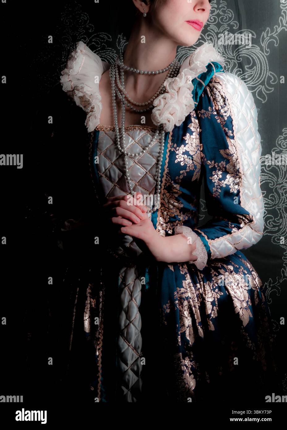 Une femme dans un costume historique, peut-être de l'époque de la Renaissance, est représentée dans un plan de studio. Elle porte une robe bleu foncé avec PA floral or Banque D'Images