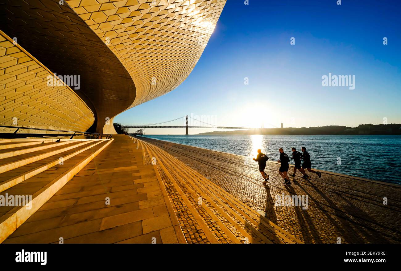 Lisbonne, Portugal. Joggers tôt le matin au bord de la rivière Tage à côté du musée moderne MAAT. Ponte de 24 Abril en arrière-plan. Banque D'Images